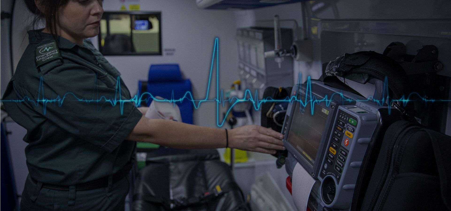 A paramedic using some electronic medical equipment. There is the medicare heartbeat image going across the centre of the screen.
