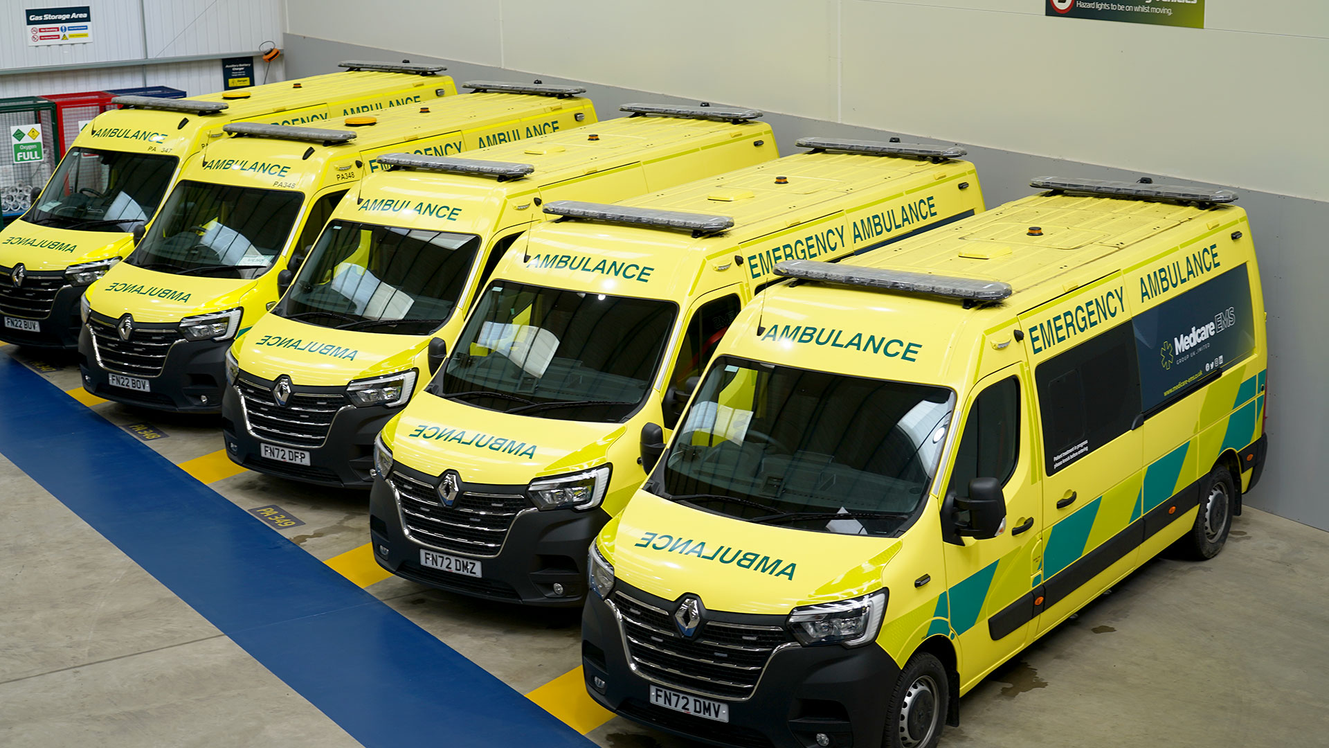 A fleet of five ambulances parked up and ready to respond, inside a warehouse.