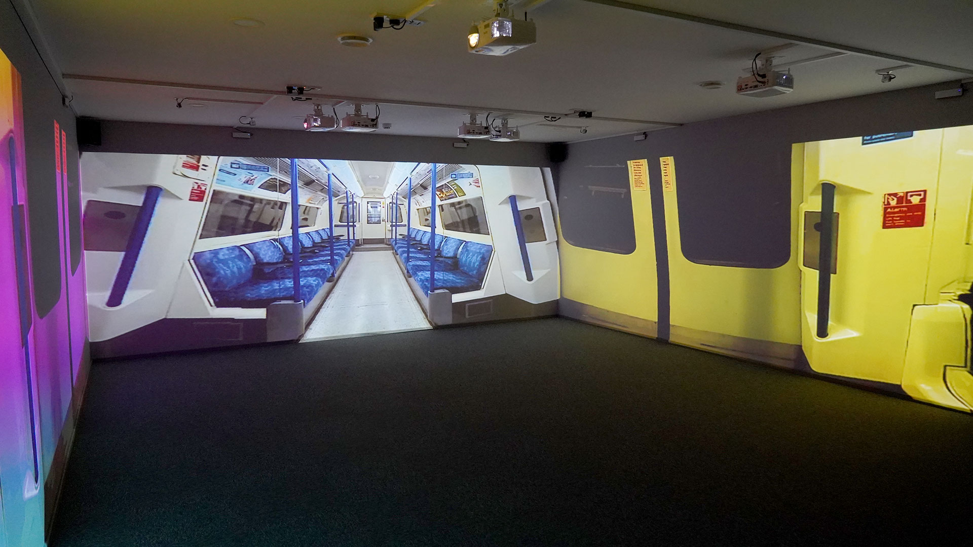 Panoramic/projector room showing London Underground appearing to be a continuous landscape however it is only a 4 sided room with projectors projecting images on three walls to give that effect. This image is showing the inside of an underground train.